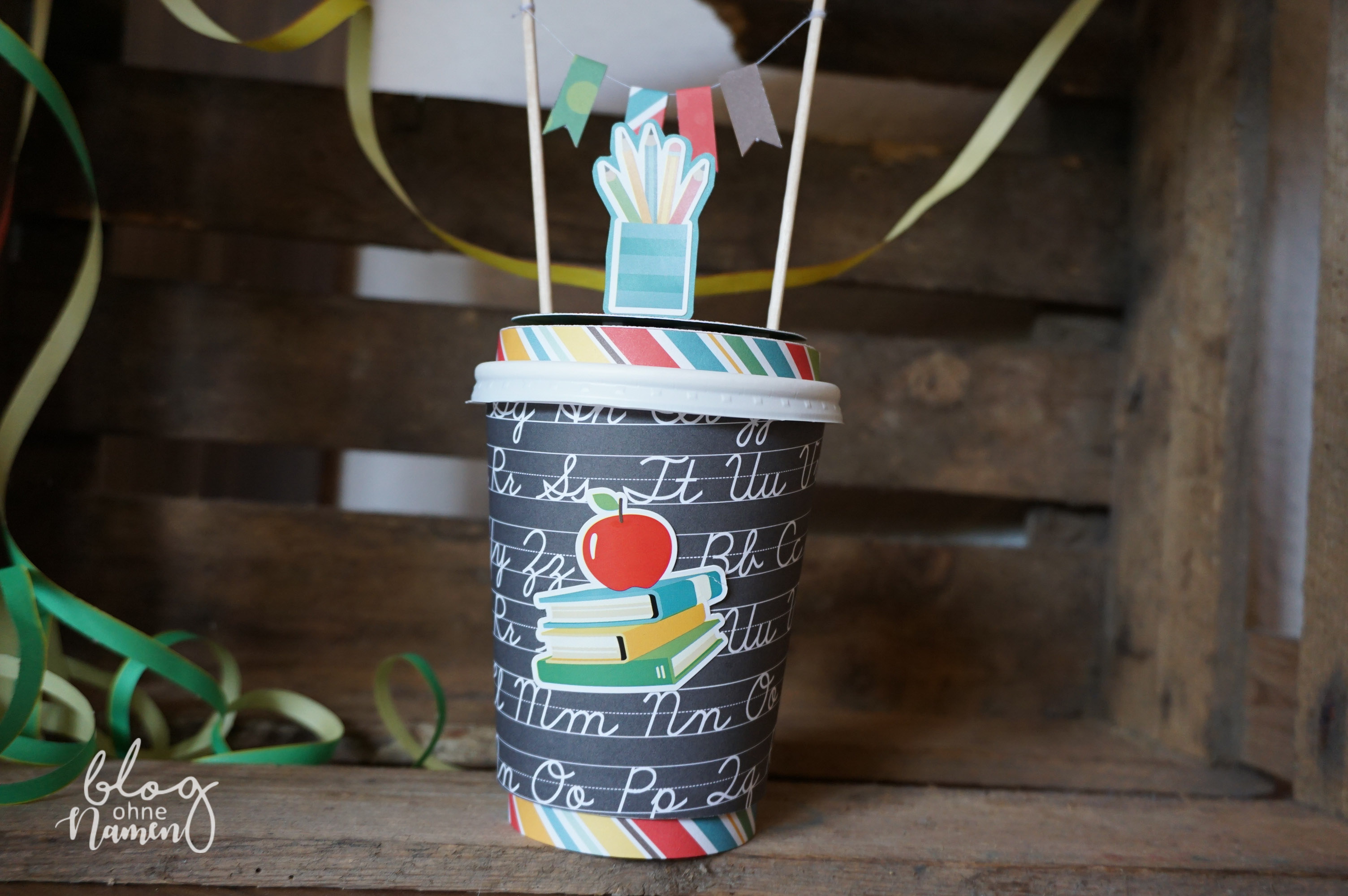 Einschulungsgeschenk mal anders: Ein gestalteter Coffee-to-go-Becher mit passender Banderole und Schuldesign-Papieren als originelle Verpackungsidee.