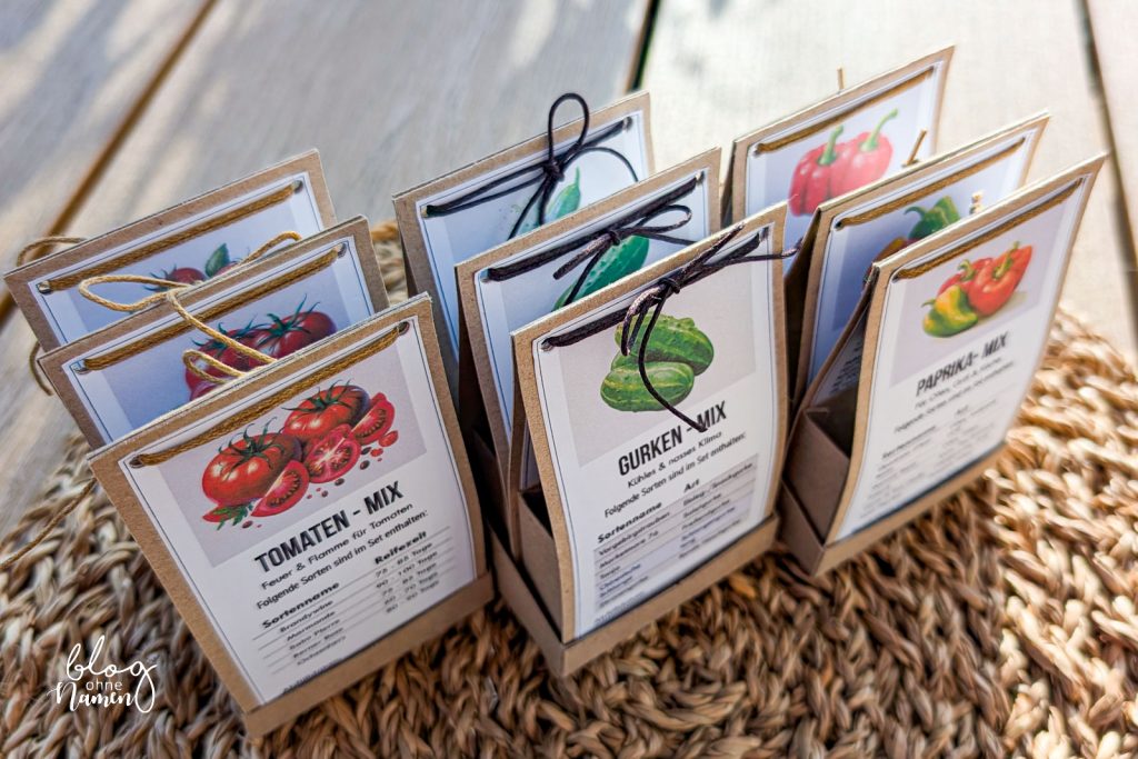 Mehrere DIY Saatgut Verpackungen aus Kraftpapier mit Tomaten-, Gurken- und Paprika-Mix, aufgefächert und mit Kordel gebunden auf einem Tisch präsentiert